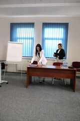 In a bright meeting room, two women work at a desk, reviewing documents and taking notes during a work session.