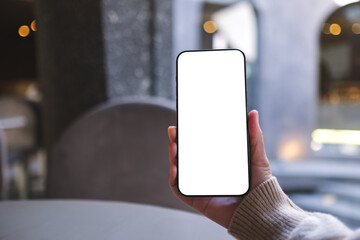 Mockup image of a woman holding and using mobile phone with blank desktop screen in cafe