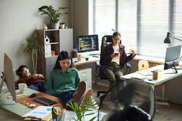 Young Asian businessmen and businesswomen working in modern office, young Asian woman sitting at desk using computer, young Asian man relaxing with headphones, young Asian woman using smartphone