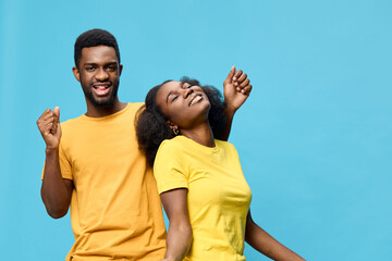 Happy young Black couple with joyful expressions, wearing bright yellow t shirts against a vibrant blue background, celebrating together in a playful moment