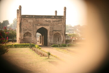 Naklejka premium The historic, weathered entrance gateway (darwaza) of an ancient Indian fort or palace. Features twin minarets, arched openings, and a large central passage.