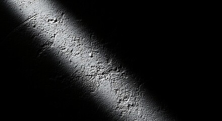 Dramatic diagonal beam of bright sunlight illuminates a textured dark surface creating a stark contrast and abstract pattern of light and shadow