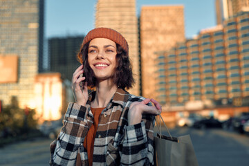 Fototapeta premium Woman on phone with shopping bags, smile framed against urban city skyline at golden hour, candid lifestyle portrait conveying authenticity, mindful living and emotional storytelling.