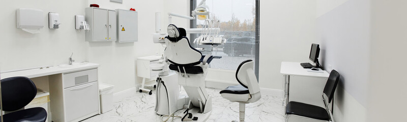 Empty dental office interior showing modern dental chair and equipment arranged near window, clean...