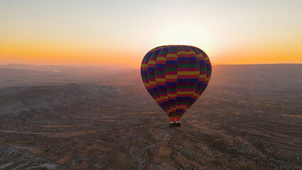 Goreme, Nevsehir, Turkey. Large colorful checkered hot air balloon with basket in backlight against the rising sun at dawn over Cappadocia. Aerial View