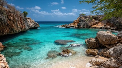 Bright turquoise waters meet rocky shores under a clear blue sky. Lush greenery surrounds the serene beach inviting visitors to enjoy the natural beauty of this tranquil location.