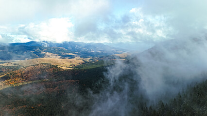 Aerial view of mist drifting above evergreen and autumn forests across a wide mountain valley. Rolling hills and distant ranges under bright sky create a serene wilderness mood for travel themes.