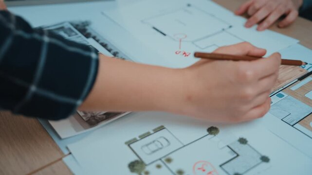 An architect hand actively sketches and marks designs on drawings, showcasing an engaging creative process amidst detailed blueprints and plans for innovative projects. SACTR