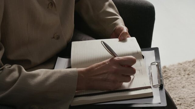 Close-up shot of unrecognisable mature female psychotherapist writing in notebook while conducting consultation during workday