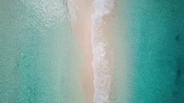 Aerial drone view of turquoise ocean waves gently hitting white sand beach, bright sunlight
