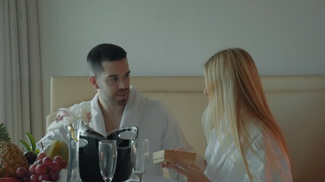 Woman joyfully opens surprise gift during romantic breakfast at home