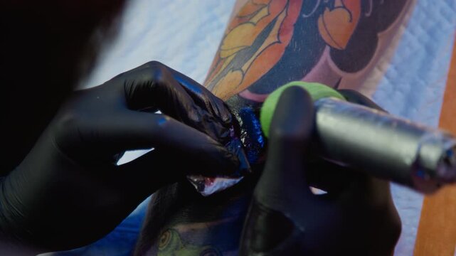 Cropped shot of hands of skilled unrecognizable tattoo artist in black sterile gloves packing color into tattoo design adding dark ink with tattoo machine