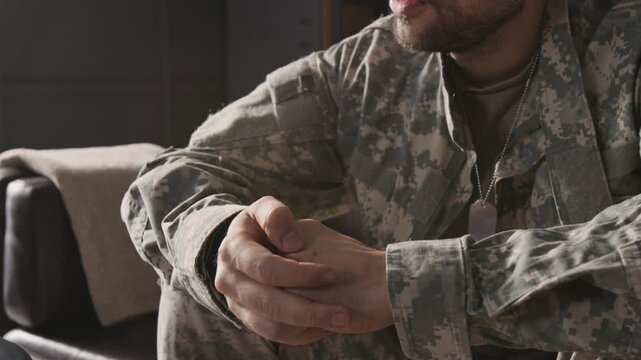Tilt up view of Caucasian bearded young military veteran wearing uniform and dog tag necklace rubbing knuckles when talking during therapy session