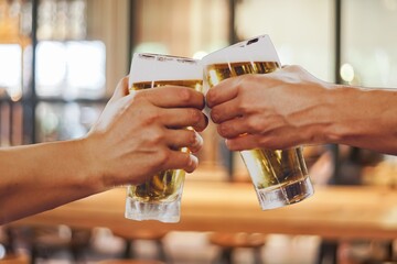 Two hands clinking glasses of beer in celebration, representing friendship and good times in a...