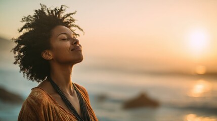 A woman stands on the beach at sunset her hair gently flowing in the breeze. She closes her eyes taking a deep breath while enjoying the peaceful surroundings and vibrant colors of the sky.