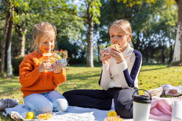 Two young girls enjoying sandwiches during a picnic in a sunny park