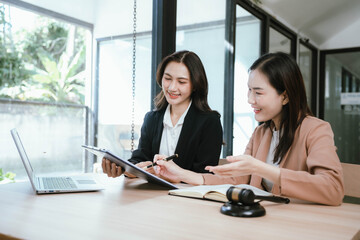 Two professional women discussing legal documents at an office desk, reviewing contracts with a...
