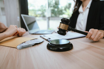 Two professional women discussing legal documents at an office desk, reviewing contracts with a laptop and gavel nearby.