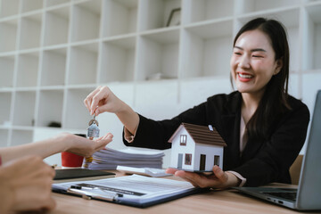 A real estate agent presenting a house model and discussing property details with a client during a contract meeting.