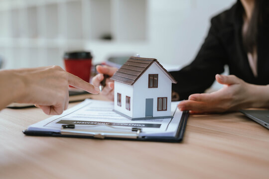 A real estate agent presenting a house model and discussing property details with a client during a contract meeting.