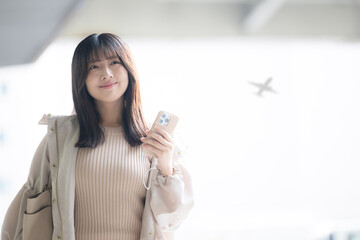飛行機が背景に見える空港や交通機関のターミナルででスマホを持つ女性の写真 © kapinon