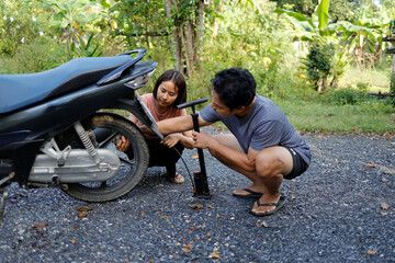 Woman and man pumping air into a motorcycle tire.