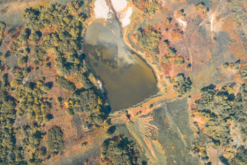 Aerial abstract of a man-made water reservoir. The irregular pond shape is defined by a geometric earth bank and surrounded by colorful autumnal vegetation, illustrating a natural boundary.