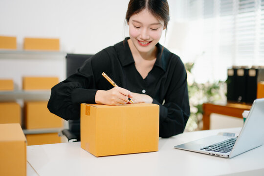 Startup small business SME, Entrepreneur owner woman using smartphone or tablet taking receive and checking online purchase shopping order to preparing pack product box.