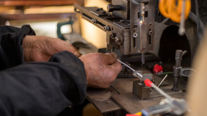 Hands performing precision work on an industrial press machine in a manufacturing workshop