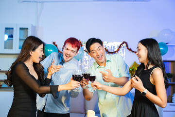 Happy young friends raise red wine glasses in a cozy indoor party setting, laughing and enjoying a festive dinner with good food, warmth, and positive vibes.
