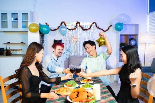 young friends feeding each other, laughing, and enjoying wine and food at a cozy indoor party with colorful decorations and a joyful vibe. - Powered by Adobe