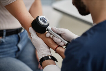 Woman undergoing skin examination by male dermatologist using dermatoscope on forearm, medical professional wearing gloves performing diagnostic procedure