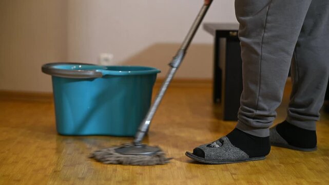 Man cleaning wooden floor with mop and bucket at home. Domestic housekeeping, wet cleaning and household chores.