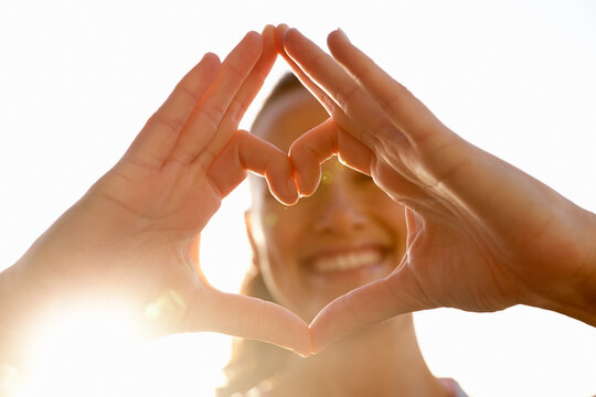 Flare, woman and happy with heart hands outdoor for appreciation, thank you and gratitude. Gesture, person and smile with love emoji for kindness, motivation symbol and sign of support with sunlight