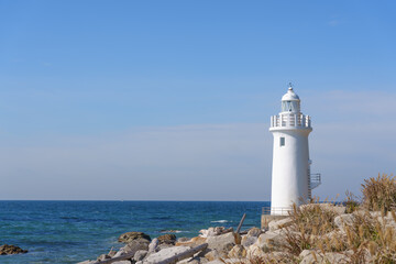The beautiful white Cape Irago Lighthouse standing tall on the rocky coastline under a clear blue sky, overlooking the expansive Pacific Ocean.
