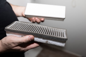 hands holding dirty cabin filter, homeowner inspecting used filter beside sealed replacement box in garage,