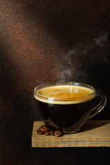 Ray of light falls on transparent cup of coffee with beans scattered around it against brown background
