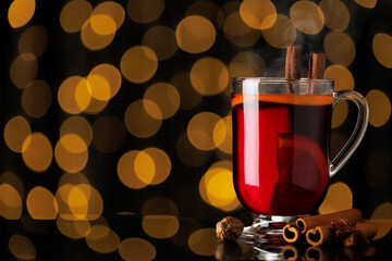steaming hot mulled wine with cinnamon and anise stars in glass mug on black background with bokeh lights