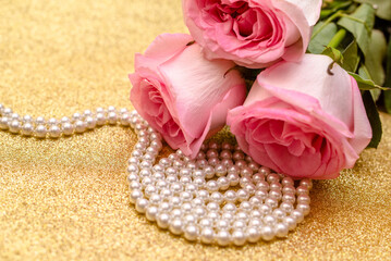 Pink rose and pearl necklace on a shiny gold background
