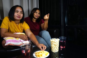 The woman in the yellow shirt is picking a snack from a plate, while her friend is talking and pointing forward.