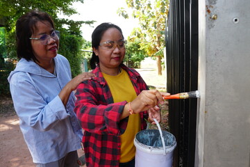 A woman in a blue shirt is gently patting the shoulder of her friend who is painting the fence with...