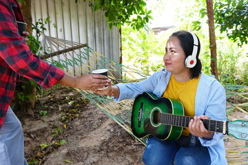 A hand is offering a cup of coffee or drink to a woman lounging in a hammock with a green acoustic...
