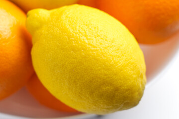 Fresh yellow lemon in pile of citrus oranges in bowl on a white table