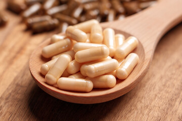 Different vitamin pills placed in wooden spoon and scattered on brown plank board close up