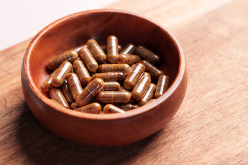 Brown vitamin capsules in wooden bowl on plank board. Natural herbal supplements