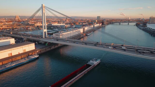 Golden Hour Aerial of Mannheim Rhein Bridge: Barge Navigating Industrial Harbor and City Skyline Traffic at Sunset, Germany