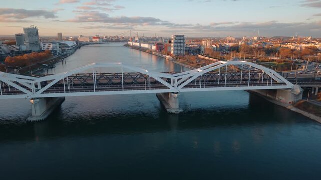 Close Aerial Tracking of Rhine Barge: Cargo Ship Sailing under Mannheim Bridge with Sunset Light and Industrial Harbor Infrastructure, Germany