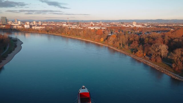 Wide Aerial of Rhine River near Mannheim: Cargo Ship Navigating City Waterfront with Autumn Colors and Sunset Skyline Panorama, Germany