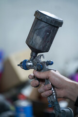 A close-up of a paint sprayer in the hand of a car mechanic