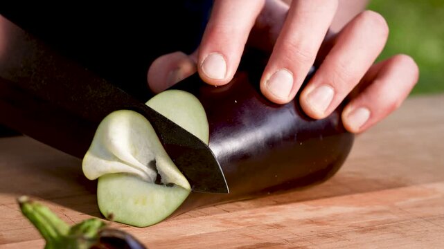 Horizontal slow-motion close-up of an eggplant slice being cut too thin and breaking apart in an outdoor kitchen. Detailed blade motion and natural textures.